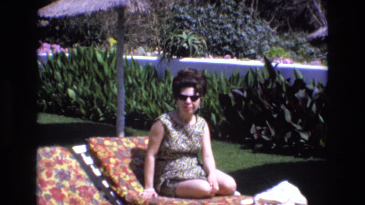 Woman seated on a lounge chair with garden foliage and a white wall behind her.