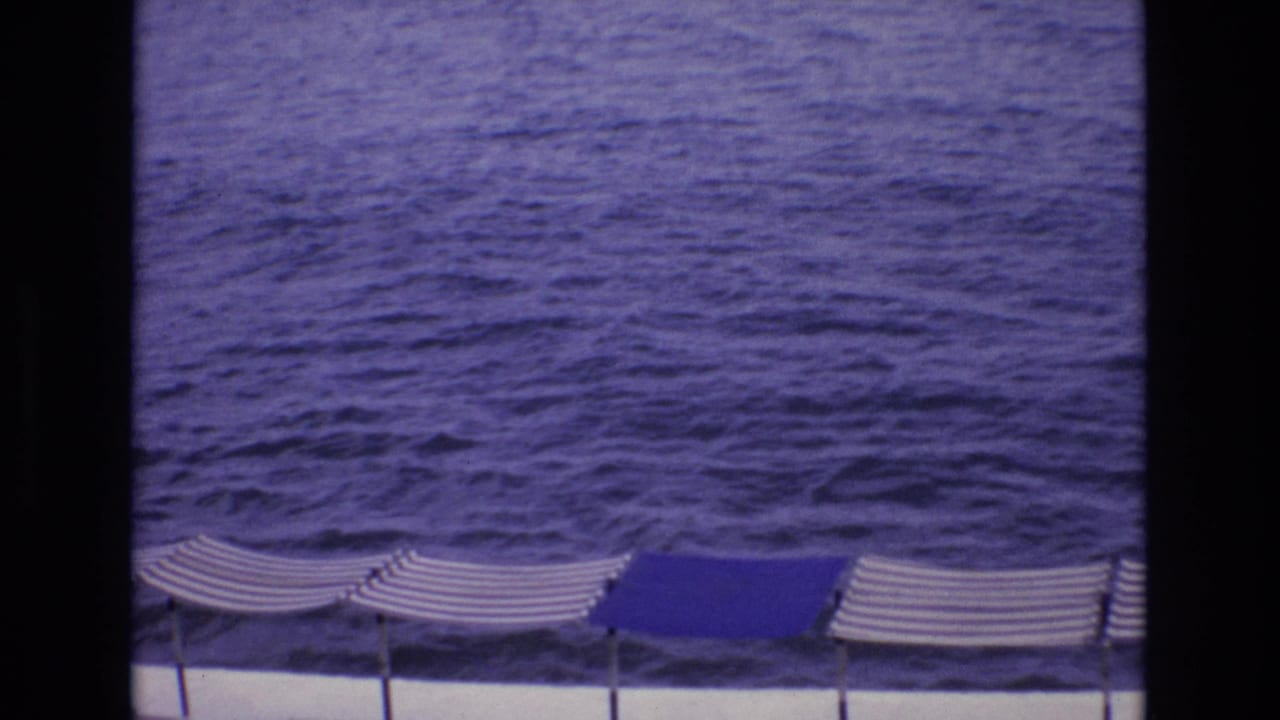 1972 Spain 8mm frame showing dark blue ocean water with striped beach umbrellas along the lower edge and dark film borders.