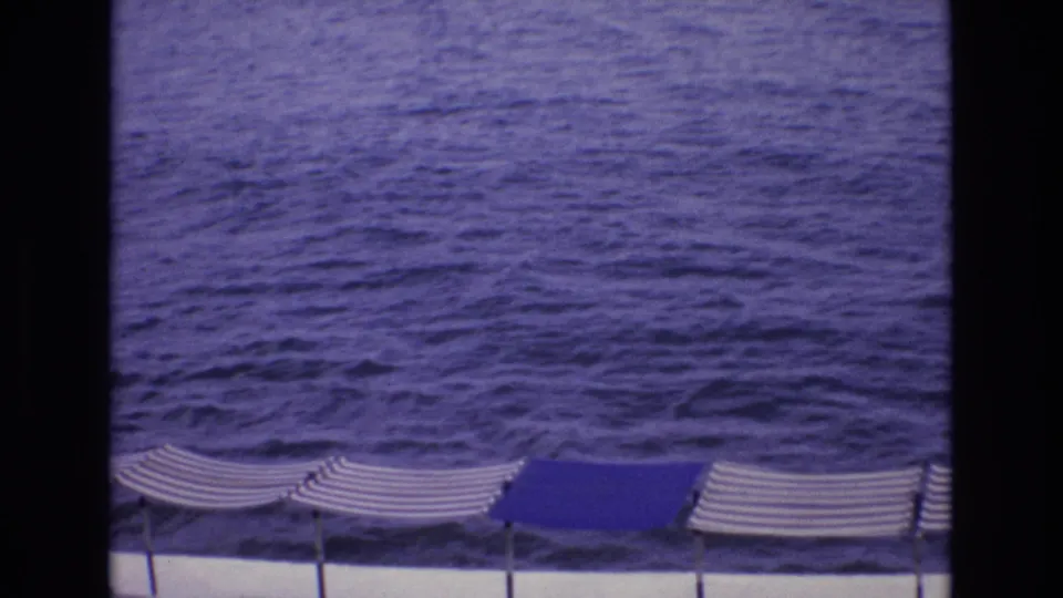 1972 Spain 8mm frame showing dark blue ocean water with striped beach umbrellas along the lower edge and dark film borders.
