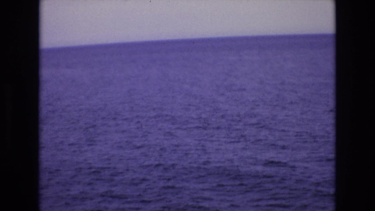 1972 Spain 8mm frame showing a wide purple-blue ocean view beneath a pale sky, bordered by dark film edges.