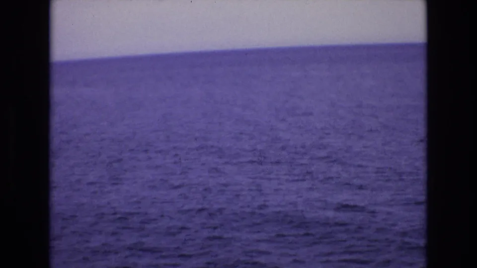 1972 Spain 8mm frame showing a wide purple-blue ocean view beneath a pale sky, bordered by dark film edges.