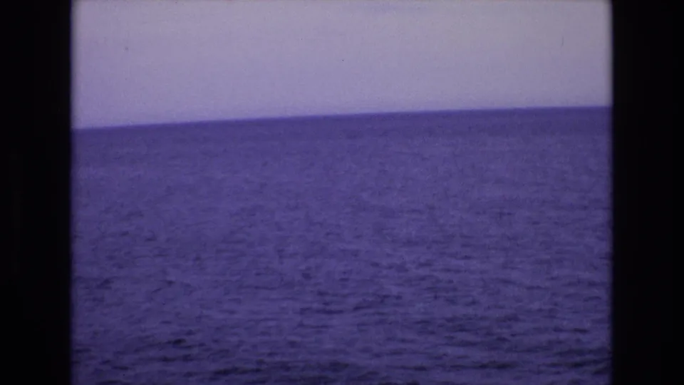 A wide 8mm home-movie view of the Spanish coast in 1972, showing open water and a pale sky with aged color shift.