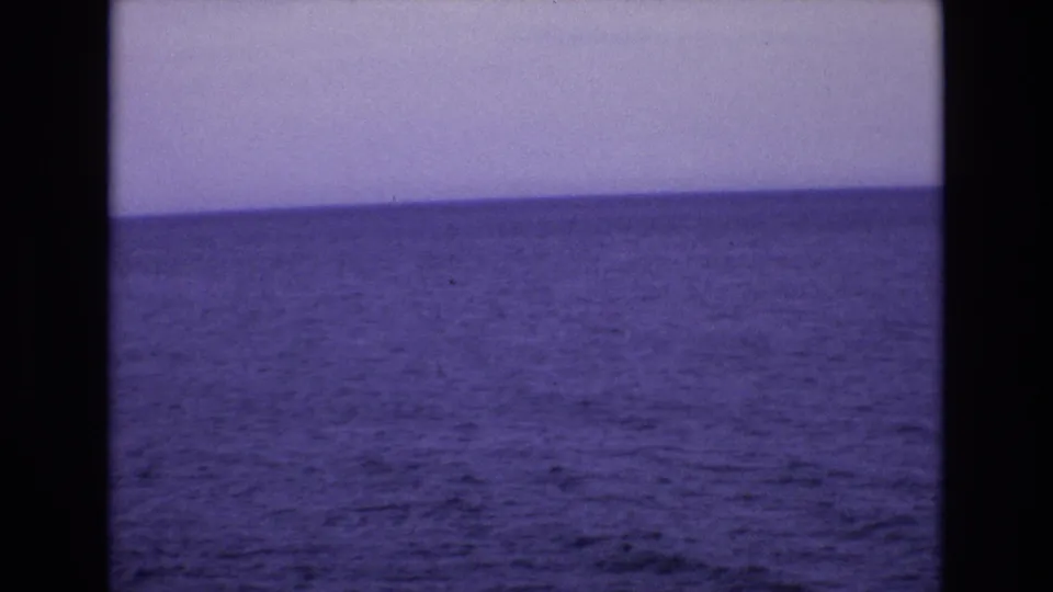 1972 Spain travel footage frame with a quiet expanse of ocean, pale sky, soft focus, and dark 8mm scan borders.