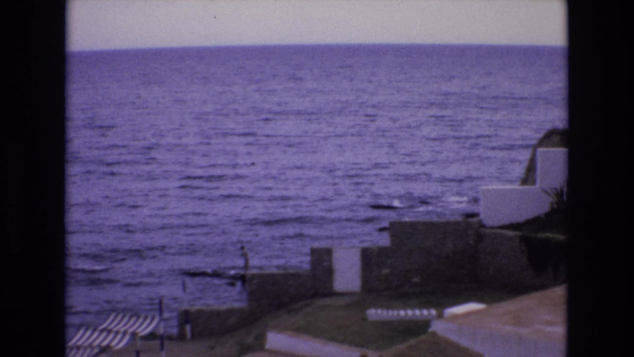 Purple-tinted sea with coastal walls, white structures, and a small figure near the water.