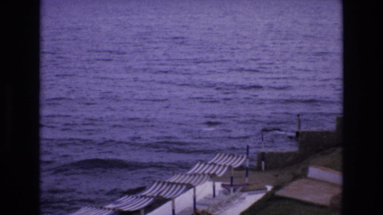 Coastal water and striped umbrellas beside a stone promenade.