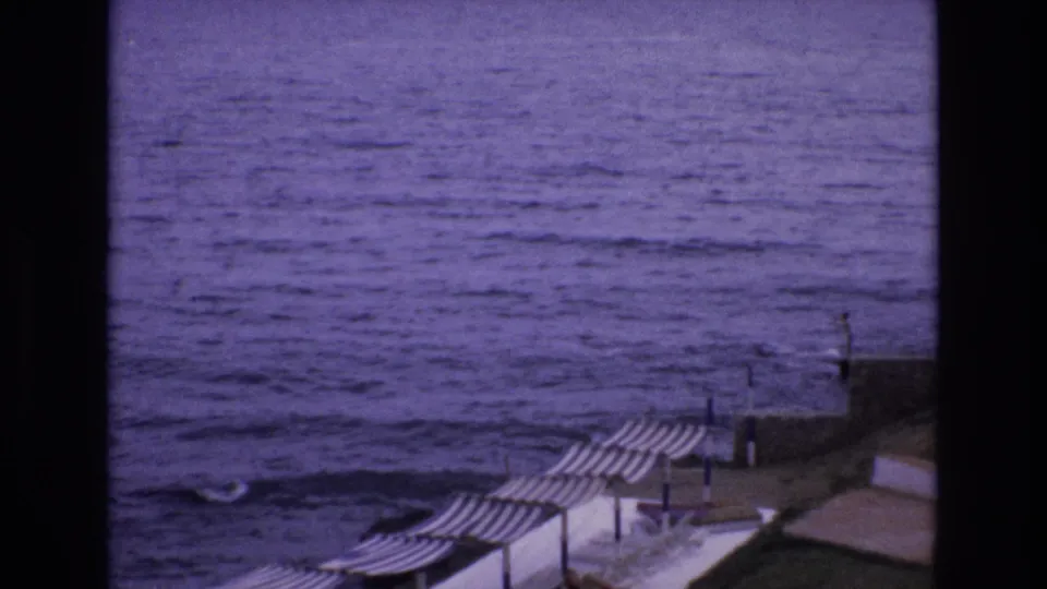 Soft 8mm frame of the Spanish coast with rippled sea and striped beach umbrellas at the lower edge of the promenade.