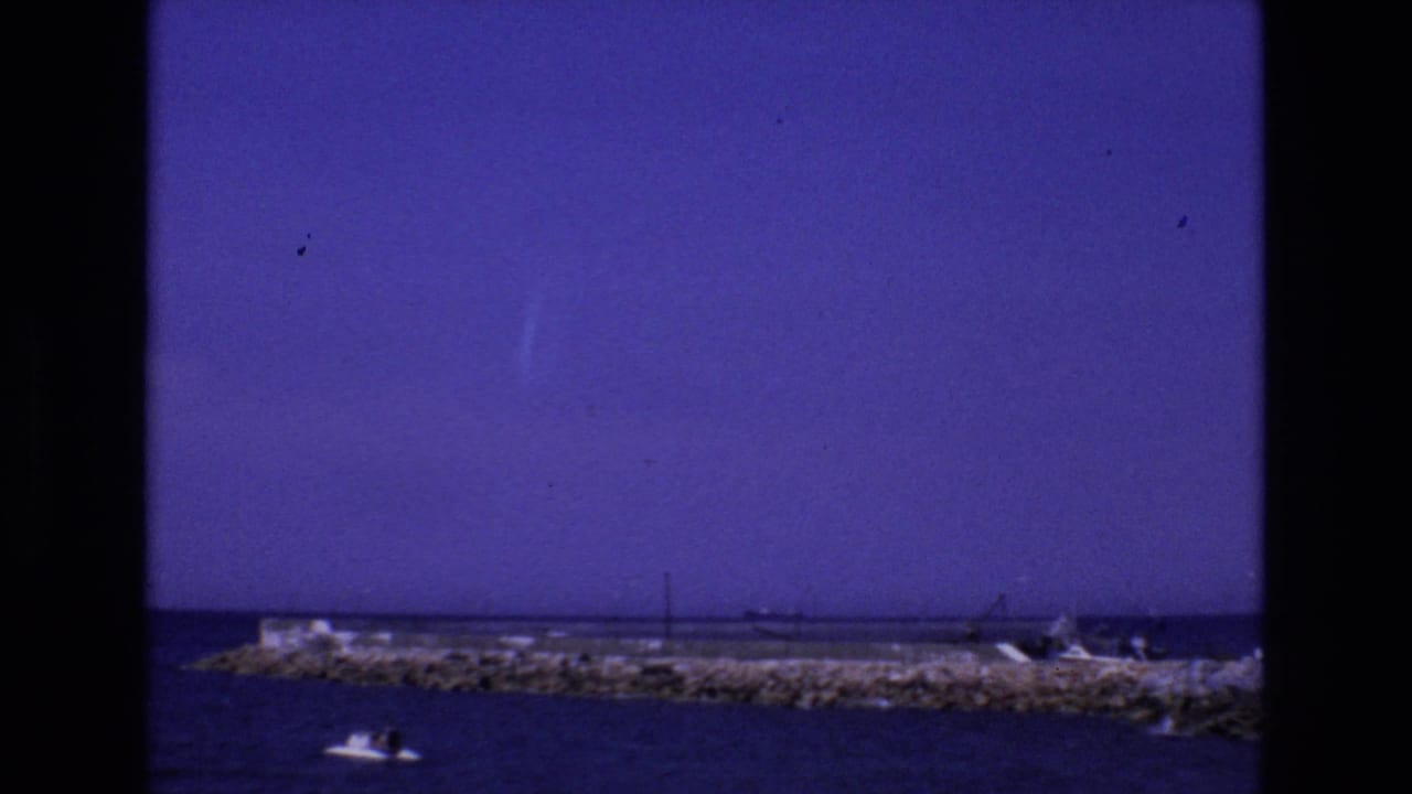 Rocky breakwater and small motorboat on calm sea beneath a blue-purple sky.