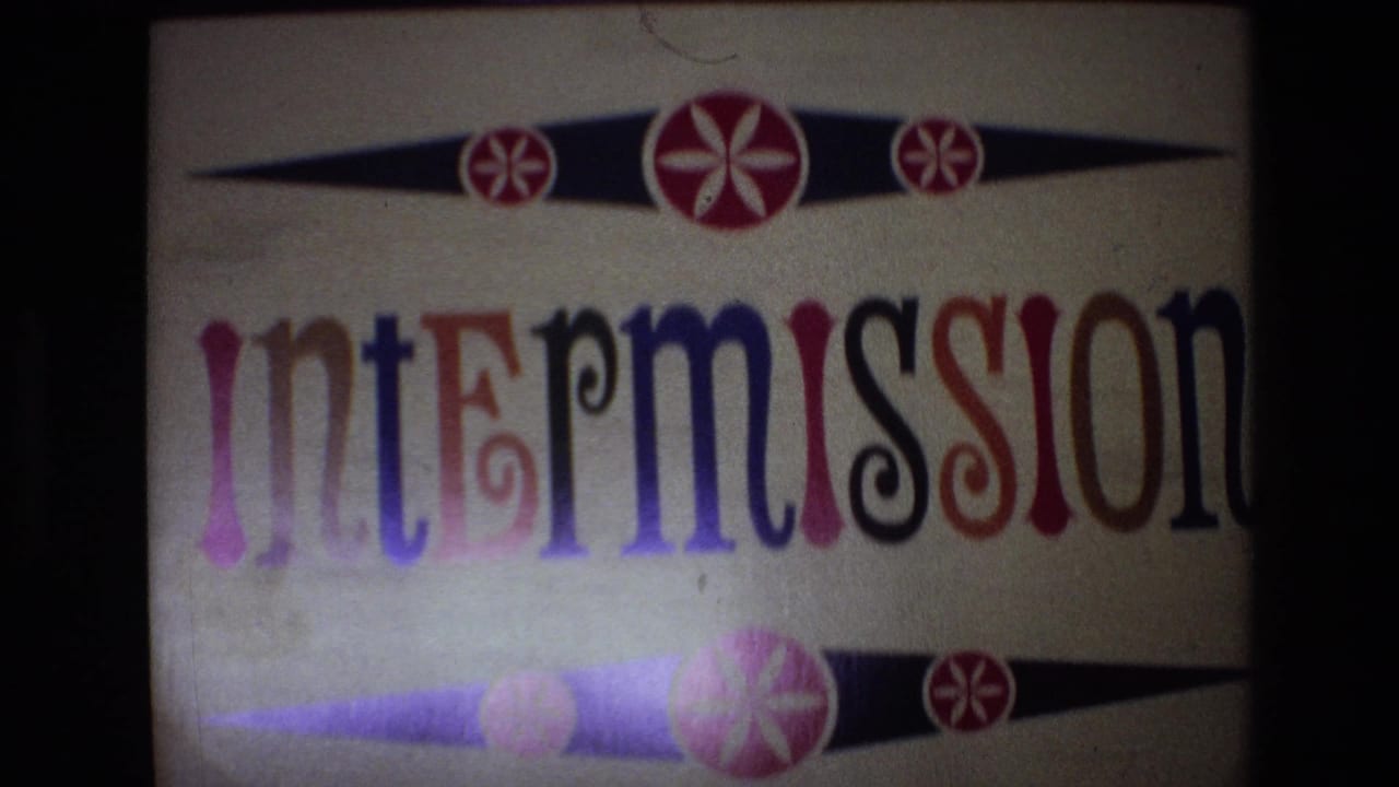 1972 Spain 8mm frame showing a projected intermission title card with multicolored serif lettering, black tapered bands, and red-and-white floral motifs.