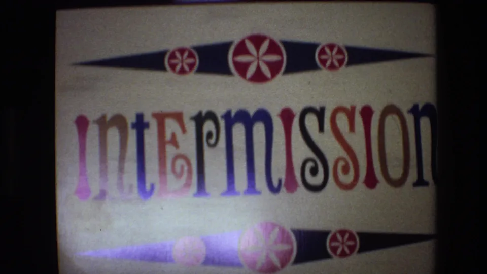 1972 Spain 8mm frame showing the projected intermission card with cropped multicolored lettering, a lower rosette band, soft exposure, and dark film-frame borders.