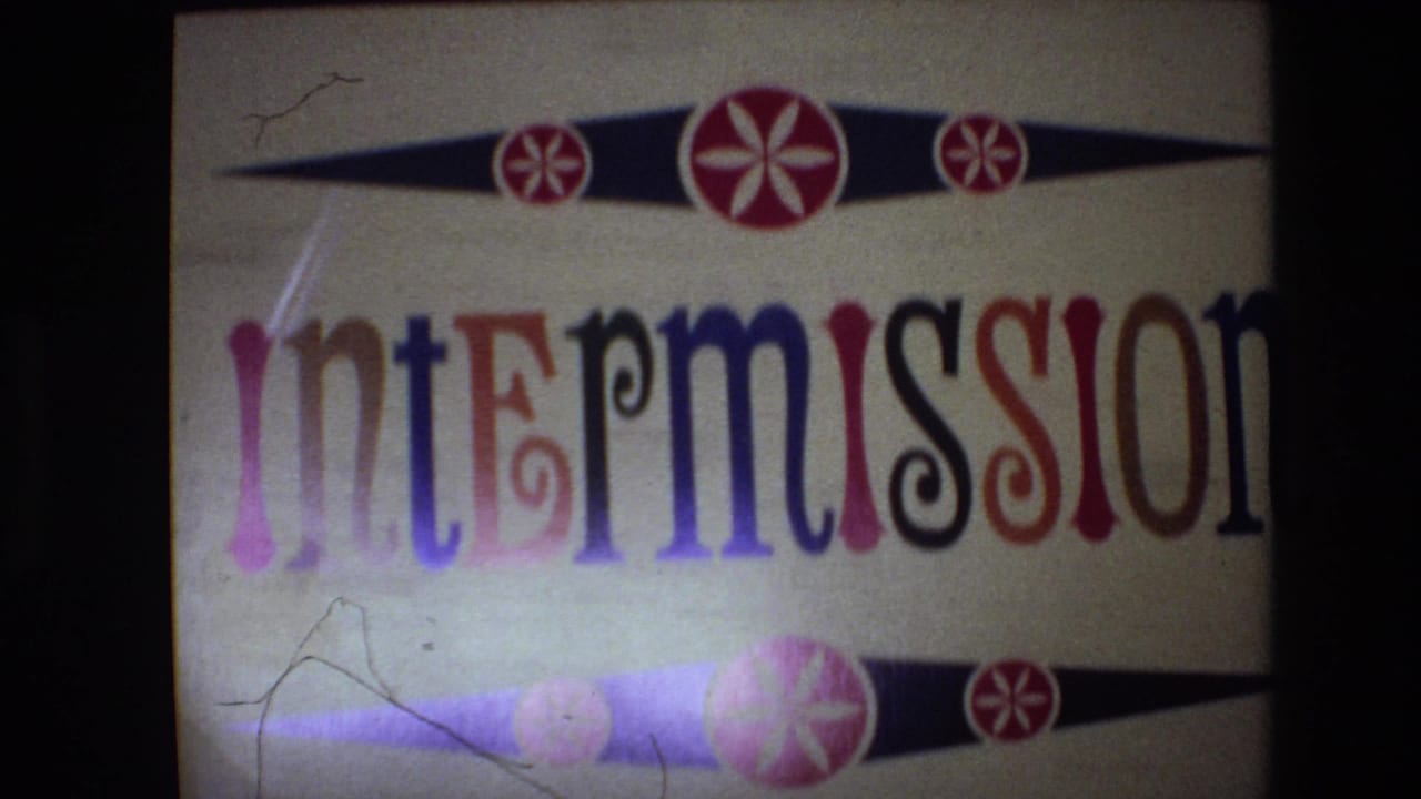 Spain 1972 8mm frame showing a projected intermission title card with multicolored lettering, black diamond ornaments, red starbursts, scratches, and dark film borders.