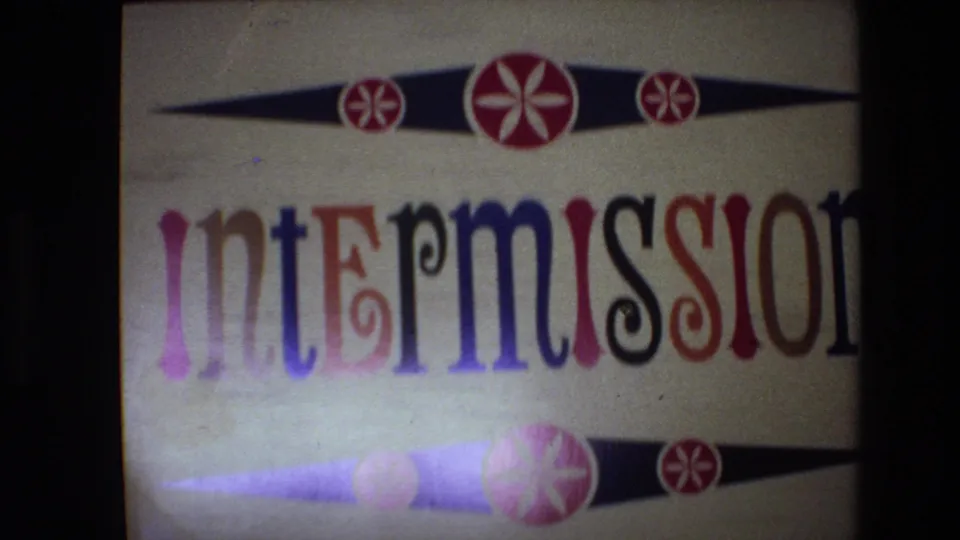 Spain 1972 8mm frame of the intermission title card near the end of the clip, showing decorative red starbursts, black horizontal shapes, partial lettering, grain, and low-light projection edges.