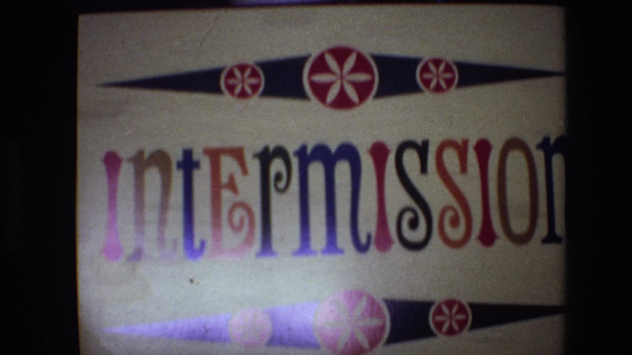 Spain 1972 8mm frame showing a handmade intermission title card with multicolored lettering, red circular motifs, and black-purple decorative bands on a cream background.