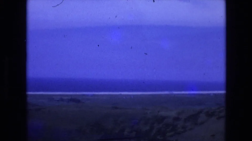 1972 Spain coastal home-movie view of a darkening beach and ocean horizon under a deep blue sky, partially bordered by the 8mm projector frame.