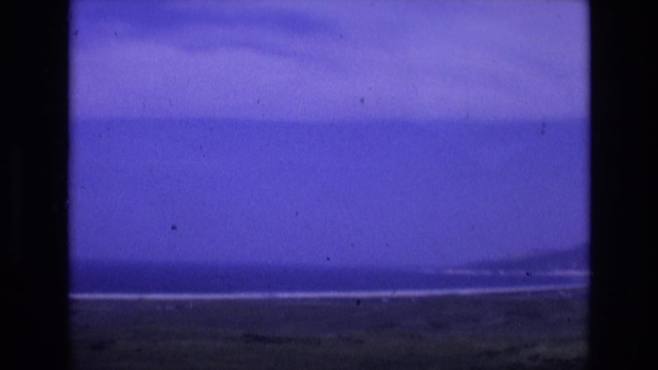 Wide ocean and shoreline view under a purple-blue sky with dark film borders.