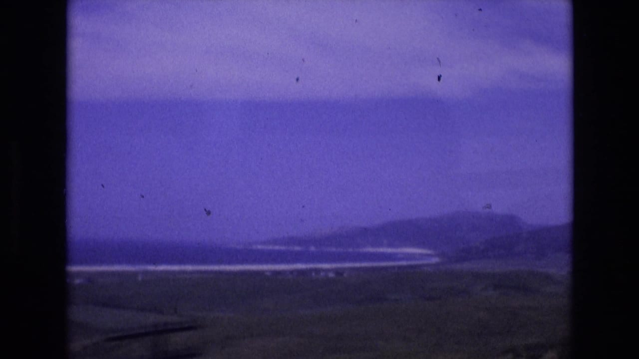Wide shoreline view with low hills, ocean and dark land in the foreground.