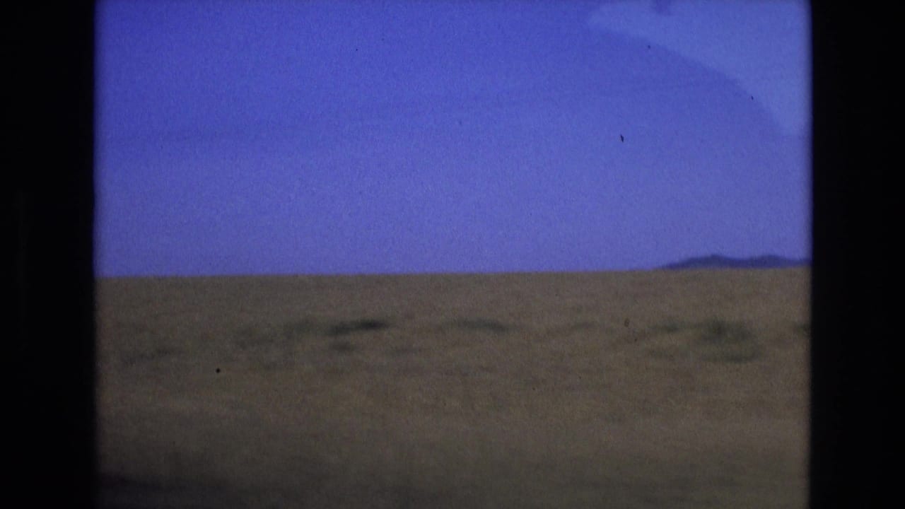 Open grassy landscape under a blue sky with low hills on the horizon.