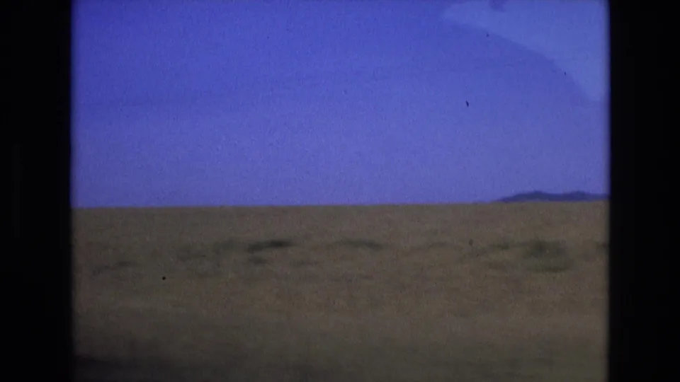 1972 Spain travel frame showing open countryside, a broad blue sky, and distant low hills, likely filmed from a moving vehicle.