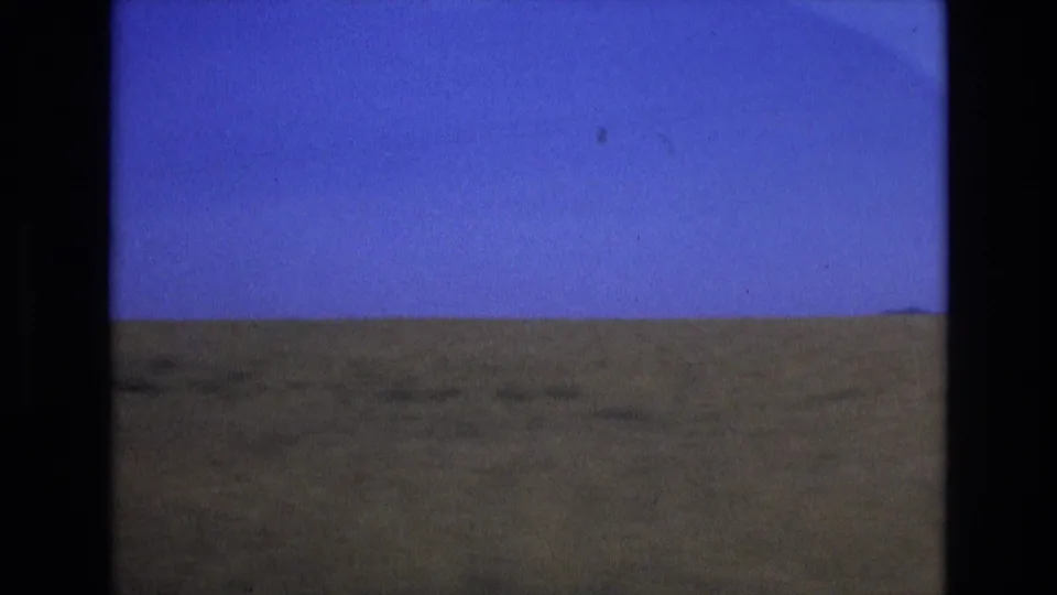1972 Spain travel frame showing a wide, open field and distant low hills under a clear blue sky in soft 8mm color.