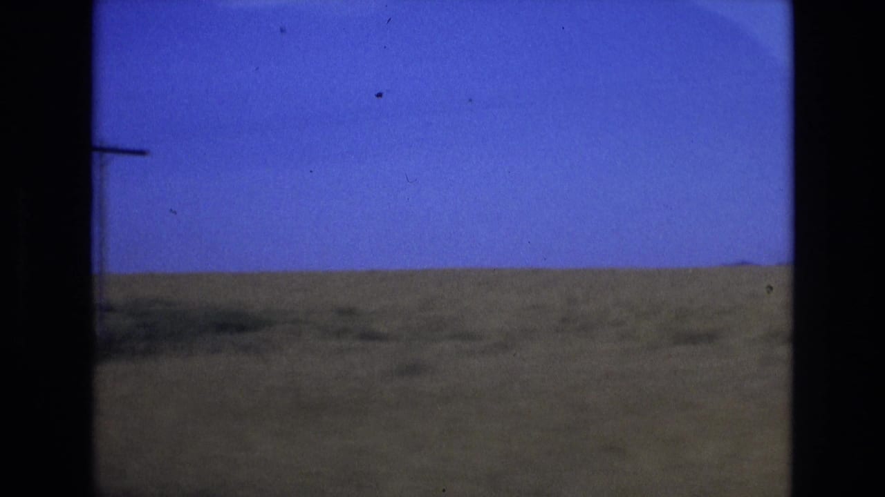 1972 Spain 8mm frame showing a low grassy plain under a saturated blue sky, with soft focus, film grain, and dark gate edges visible.