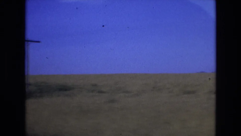 1972 Spain 8mm frame showing a low grassy plain under a saturated blue sky, with soft focus, film grain, and dark gate edges visible.