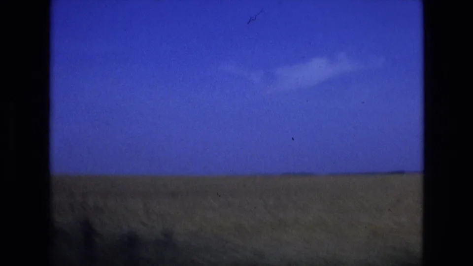 1972 Spain 8mm frame showing a small cloud in a deep blue sky above an open grassy horizon, with handheld softness and visible scan texture.