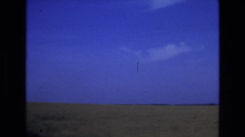1972 Spain 8mm frame showing a wide open sky, small cloud, and distant grassy plain, with dark film borders and dust marks from the original scan.