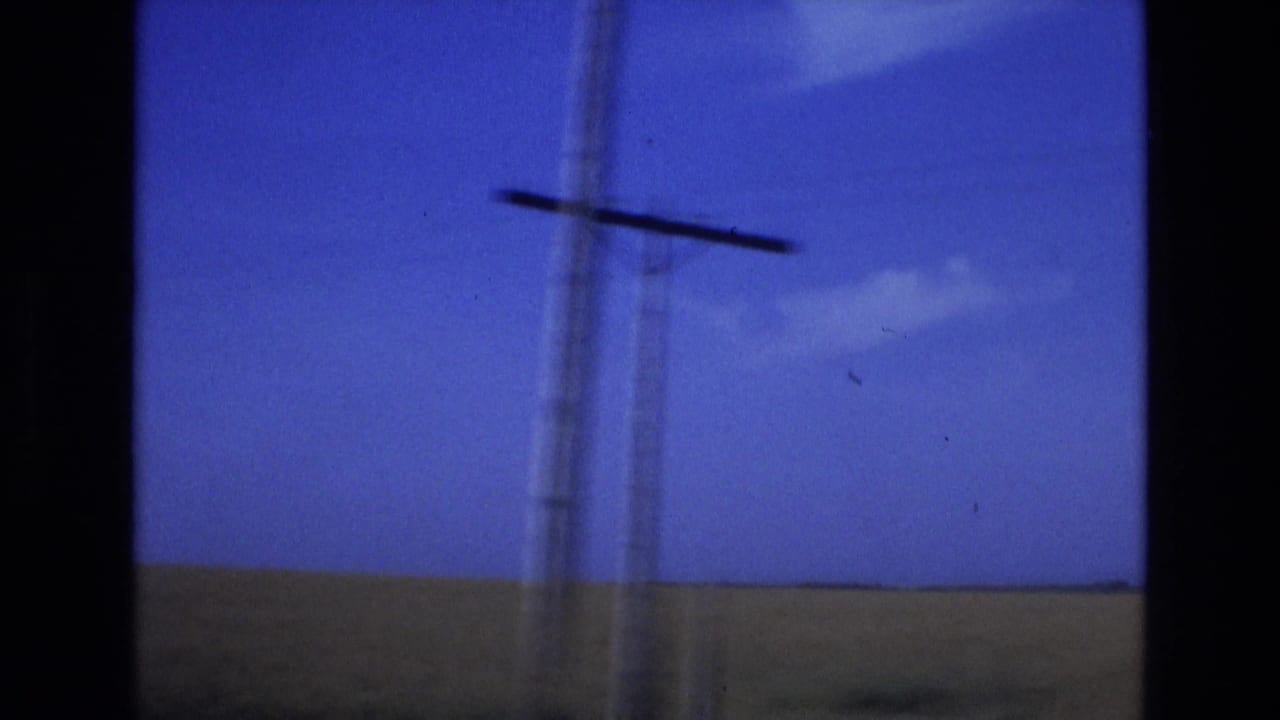 1972 Spain 8mm frame showing a roadside telephone pole blurred by vehicle motion against open fields and a blue sky.