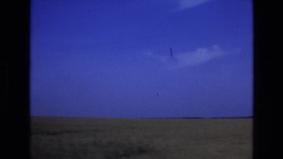 1972 Spain 8mm frame of flat rural fields stretching to the horizon beneath a saturated blue sky and a small cloud.