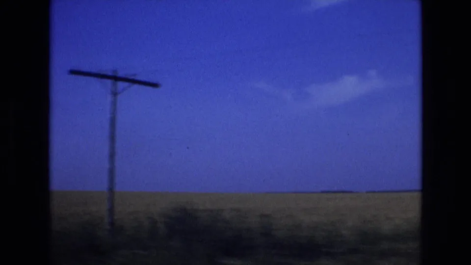 1972 Spain 8mm frame with a roadside telephone pole at left, open countryside, and a blue sky seen from a moving vehicle.