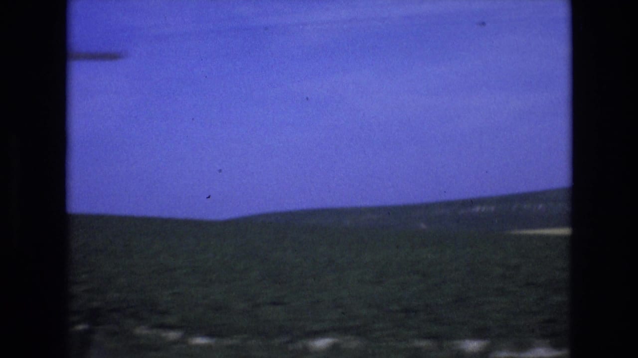 Rolling hills below a blue sky with dark vertical window framing.