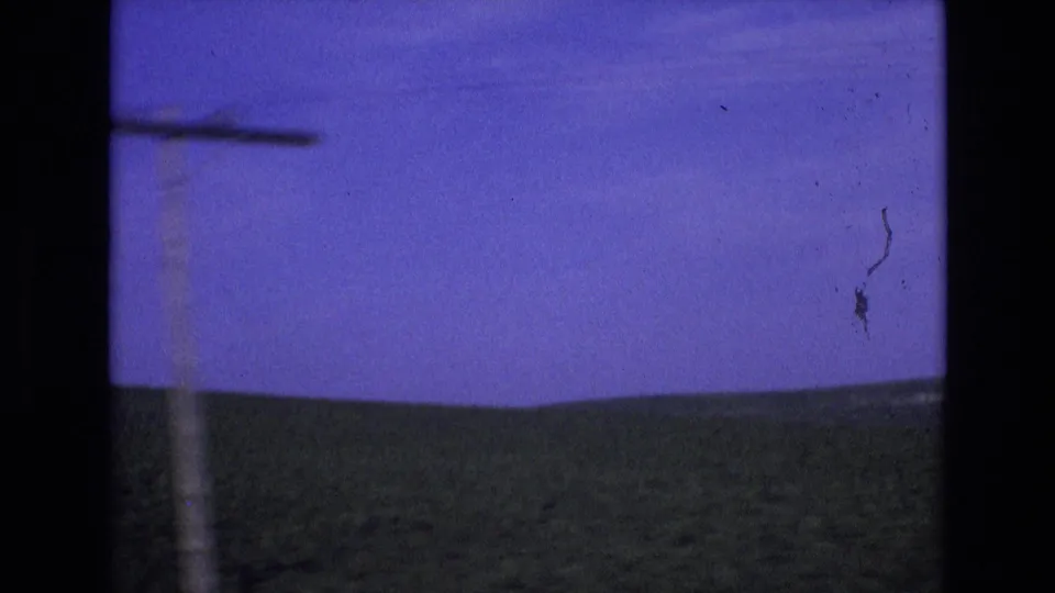 1972 Spain road-travel frame showing a roadside utility pole crossing the view, with green hills and a saturated blue sky beyond the car window.