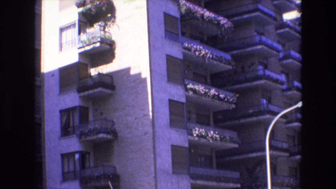Apartment balconies with flower boxes, shuttered windows, bright wall, and street lamp edge.