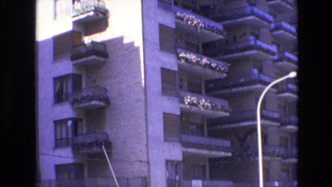 Spain, 1972, showing a tall urban apartment facade with projecting balconies, flower boxes, shuttered windows, a curved streetlamp, and shopfronts at street level.