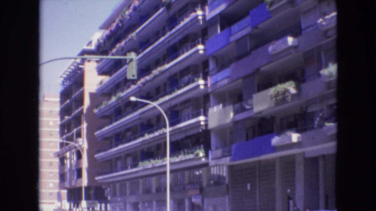 Apartment block with balconies, blue awnings, plants, curved streetlights, and a traffic signal.
