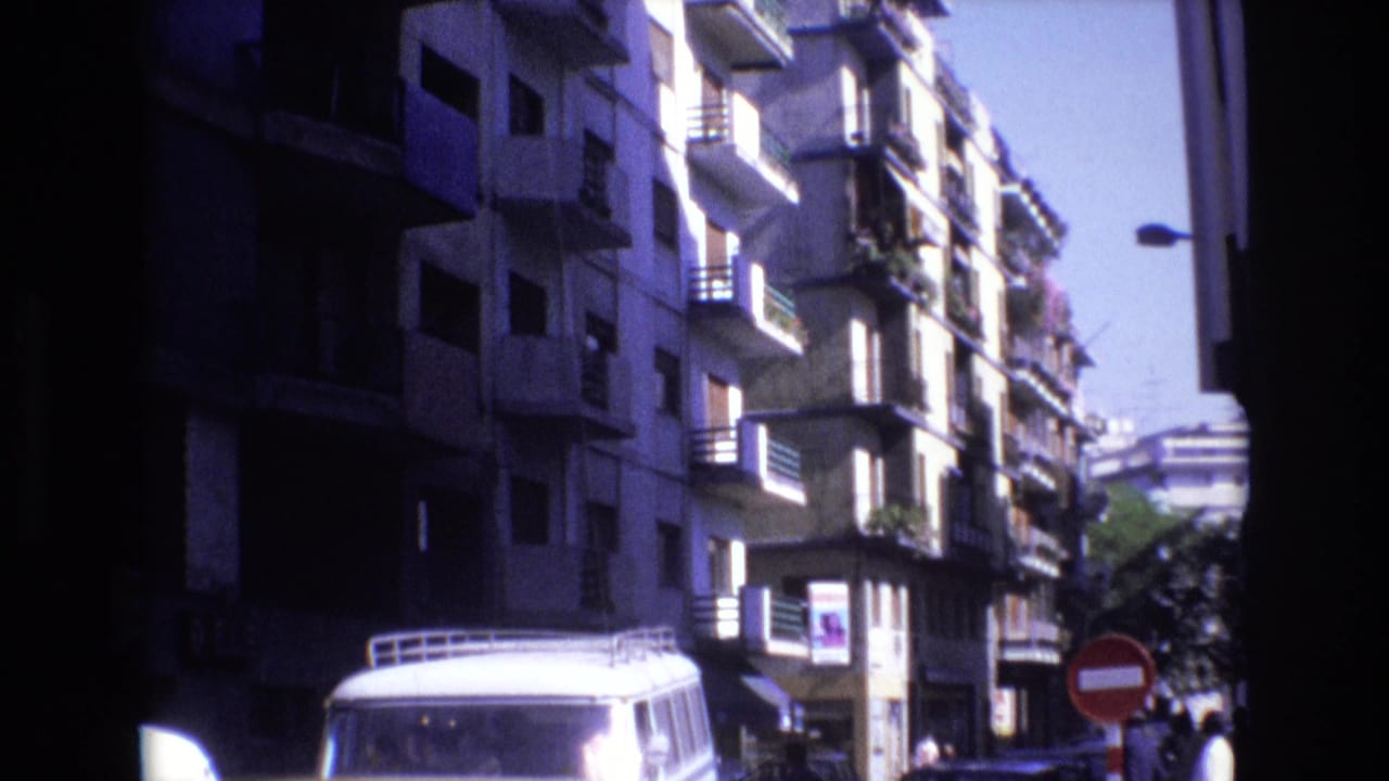 Narrow city street with apartment balconies, a white van, parked cars, and a do-not-enter sign.