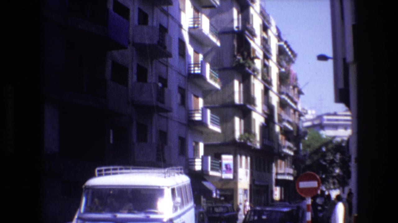A white van with a roof rack moves along a Spanish city street in the supplied 1972 footage, framed by tall apartment buildings with balconies and a red no-entry sign.
