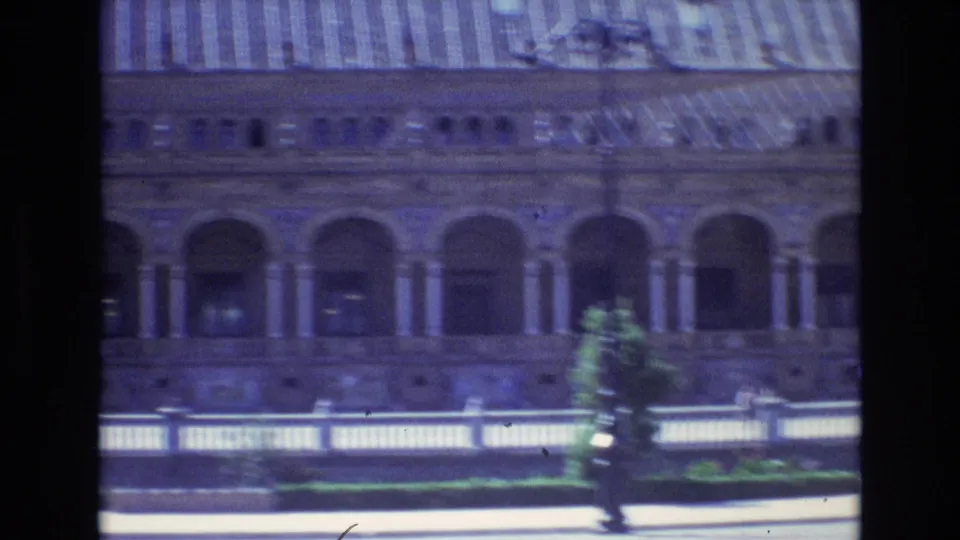 A large Spanish building exterior appears from a moving 1972 home-movie viewpoint, showing arched colonnades, a striped roof, and a pale balustrade in front.