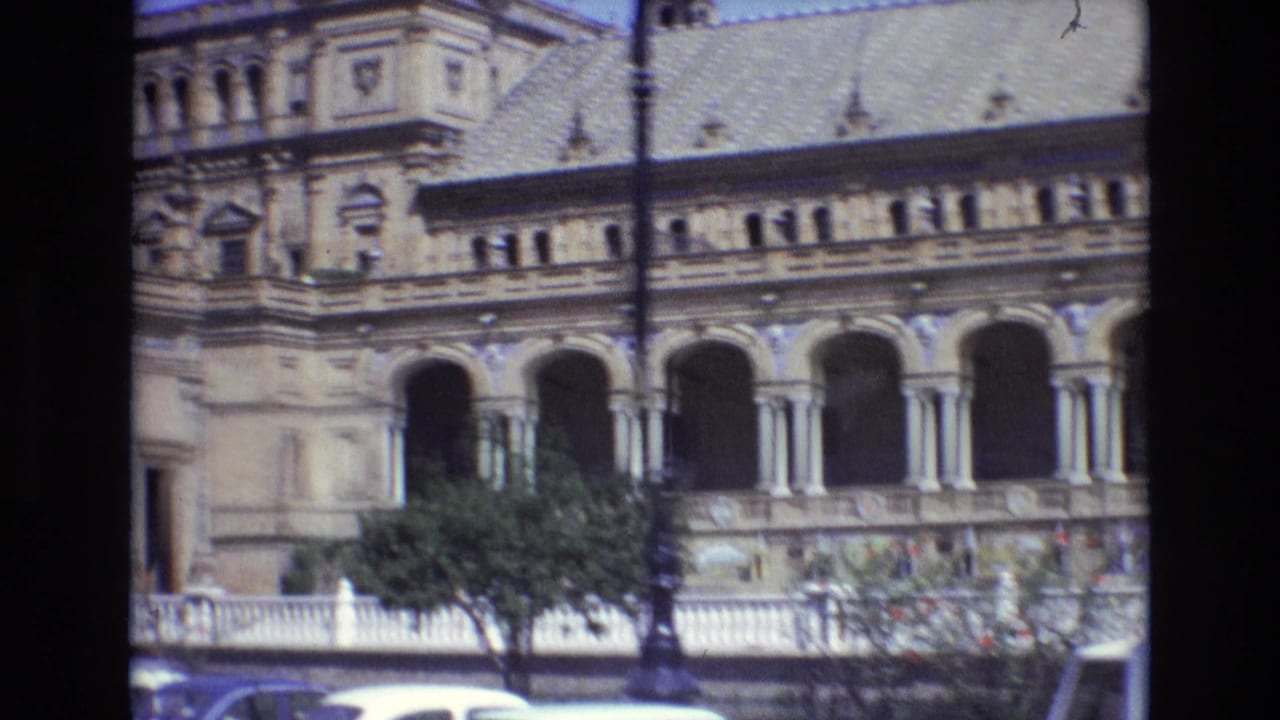 Ornate arched building facade with parked or passing cars partly visible below.