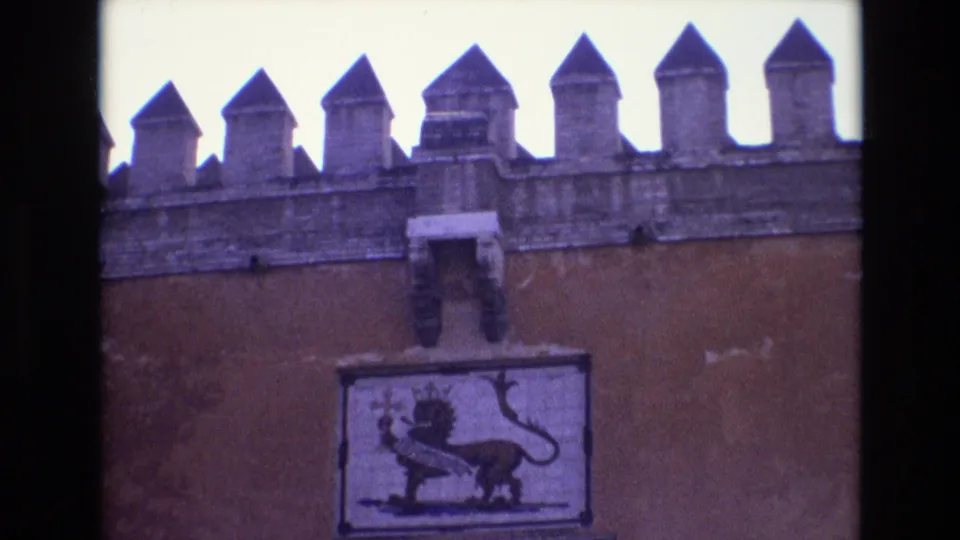 1972 Spain 8mm frame showing a crenellated historic wall and a crowned lion symbol panel above the upper part of a stone entrance.