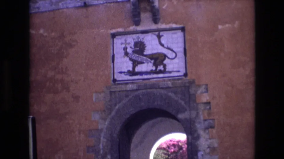 1972 Spain 8mm frame looking down from the lion symbol panel to the arched stone entrance and bright passage beyond.