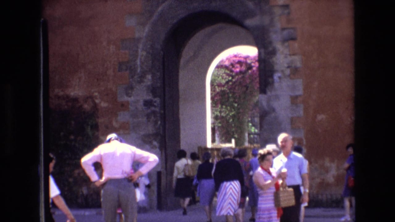 Visitors walking and standing beside a tall arched doorway with flowering plants visible beyond it.