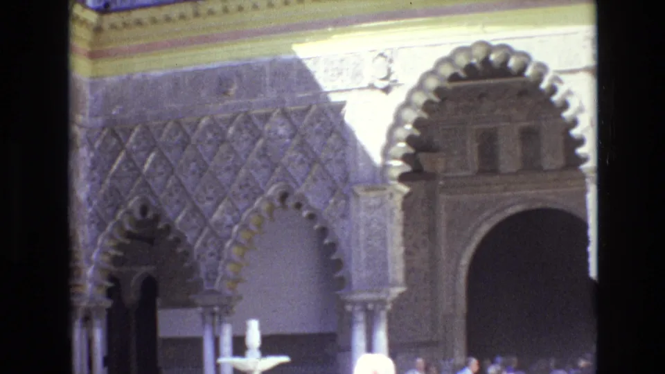 1972 Spain 8mm frame showing detailed carved arches, patterned wall surfaces, a small fountain, and visitors partly visible in a historic courtyard.