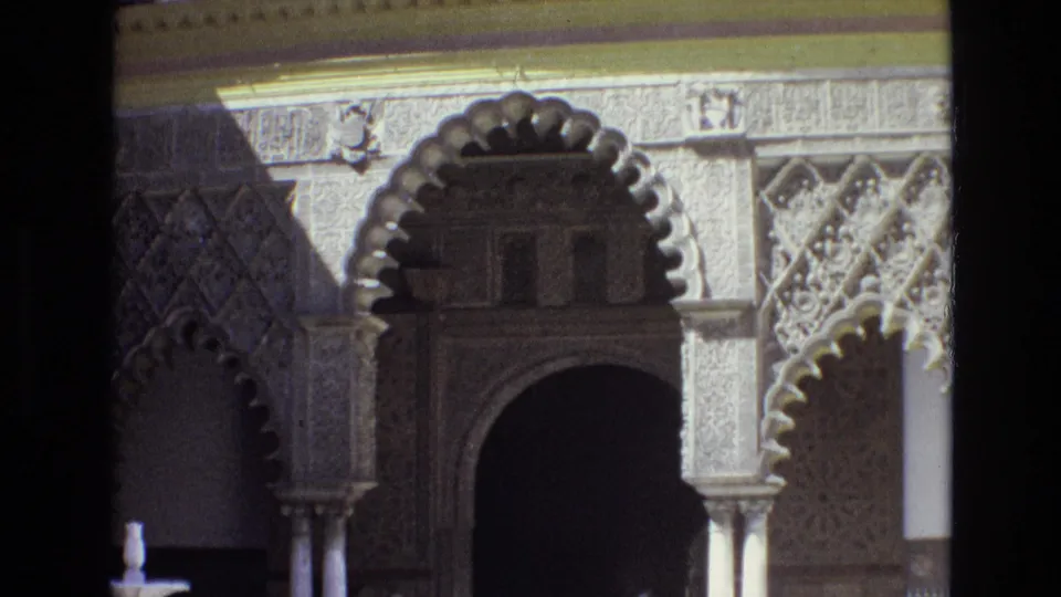 1972 Spain home-movie frame showing an ornate scalloped archway, carved stone facade, columns, and geometric decoration in strong sunlight.