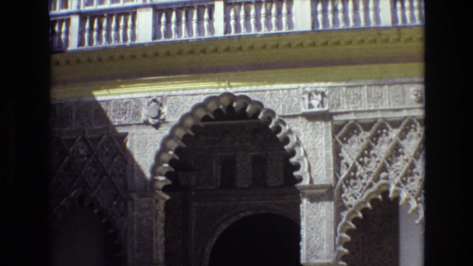 1972 Spain frame of a historic-looking decorative facade with scalloped arches, carved panels, a balcony railing, and deep shadow under the entryway.