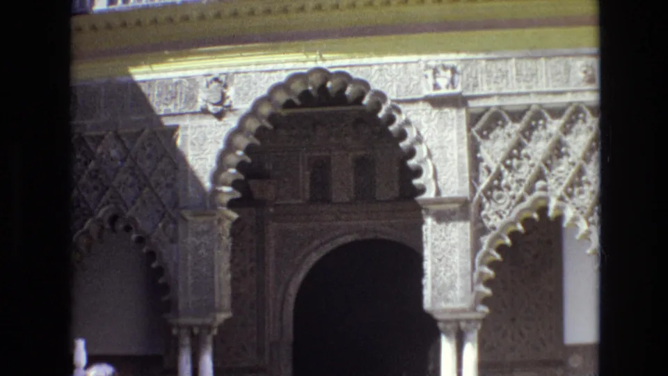 1972 Spain home-movie view centered on ornate arched stonework, slim columns, carved geometric surfaces, and a dark recessed doorway.