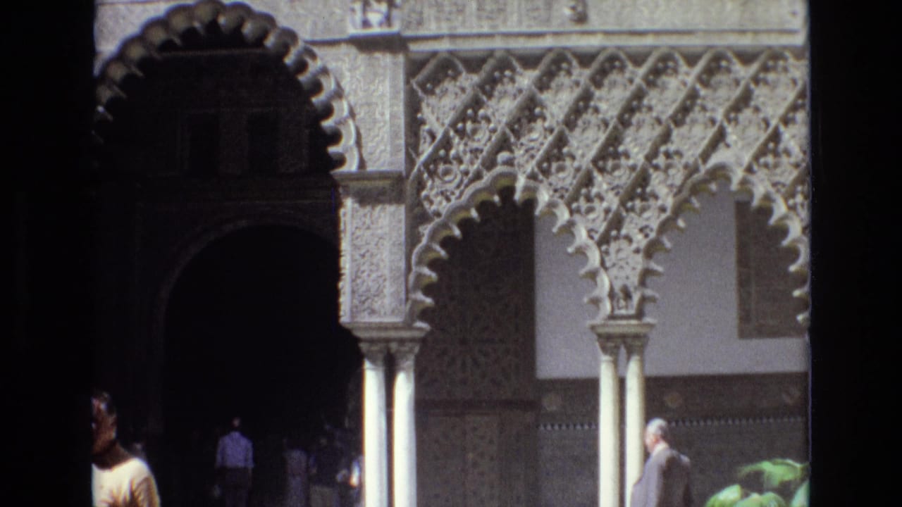 Spain 1972 home-movie frame showing visitors in a sunlit courtyard with scalloped arches, carved columns, and decorative wall panels.