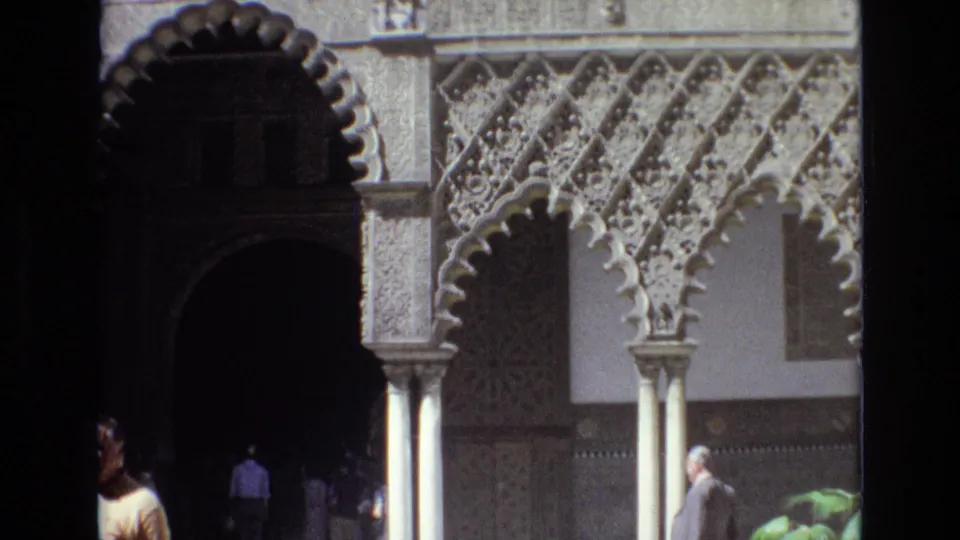 Spain 1972 home-movie frame showing visitors in a sunlit courtyard with scalloped arches, carved columns, and decorative wall panels.