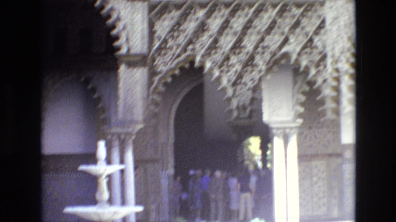 A small fountain stands before ornate arches while visitors gather near a shaded doorway.