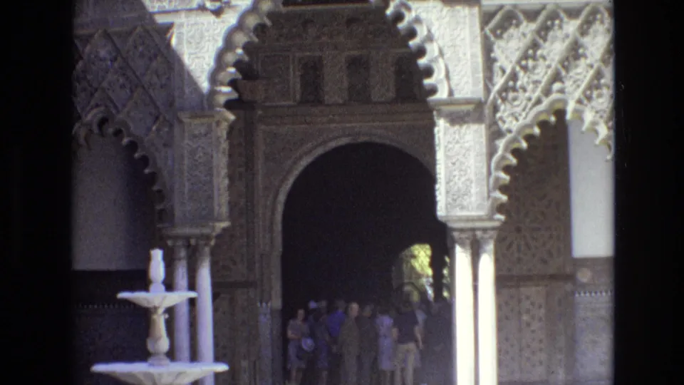 Spain 1972 home-movie view of a tiered fountain, broad scalloped arch, carved architectural details, and visitors in the shaded entrance beyond.
