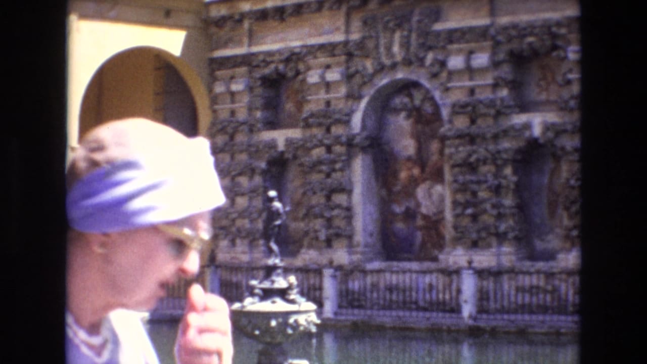 Woman in a pale head covering passes in front of a courtyard fountain and ornate wall.